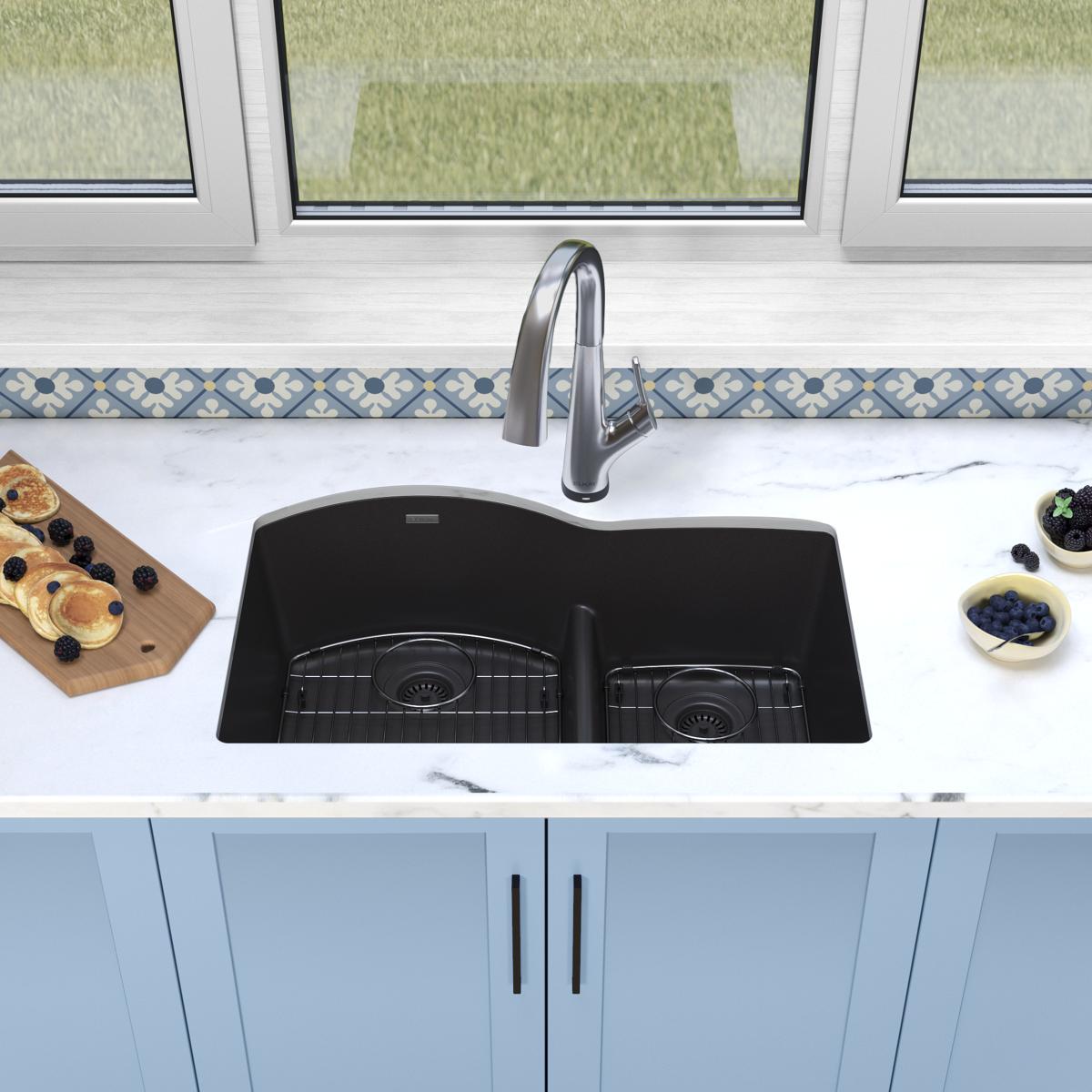 Black quartz double bowl undermount sink with chrome filtered faucet and divider installed in white countertop.