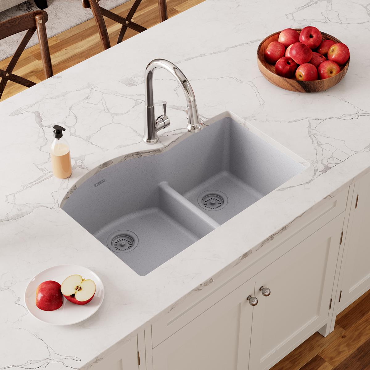 Greystone quartz double bowl undermount sink with divider installed in white marble countertop, chrome faucet visible.