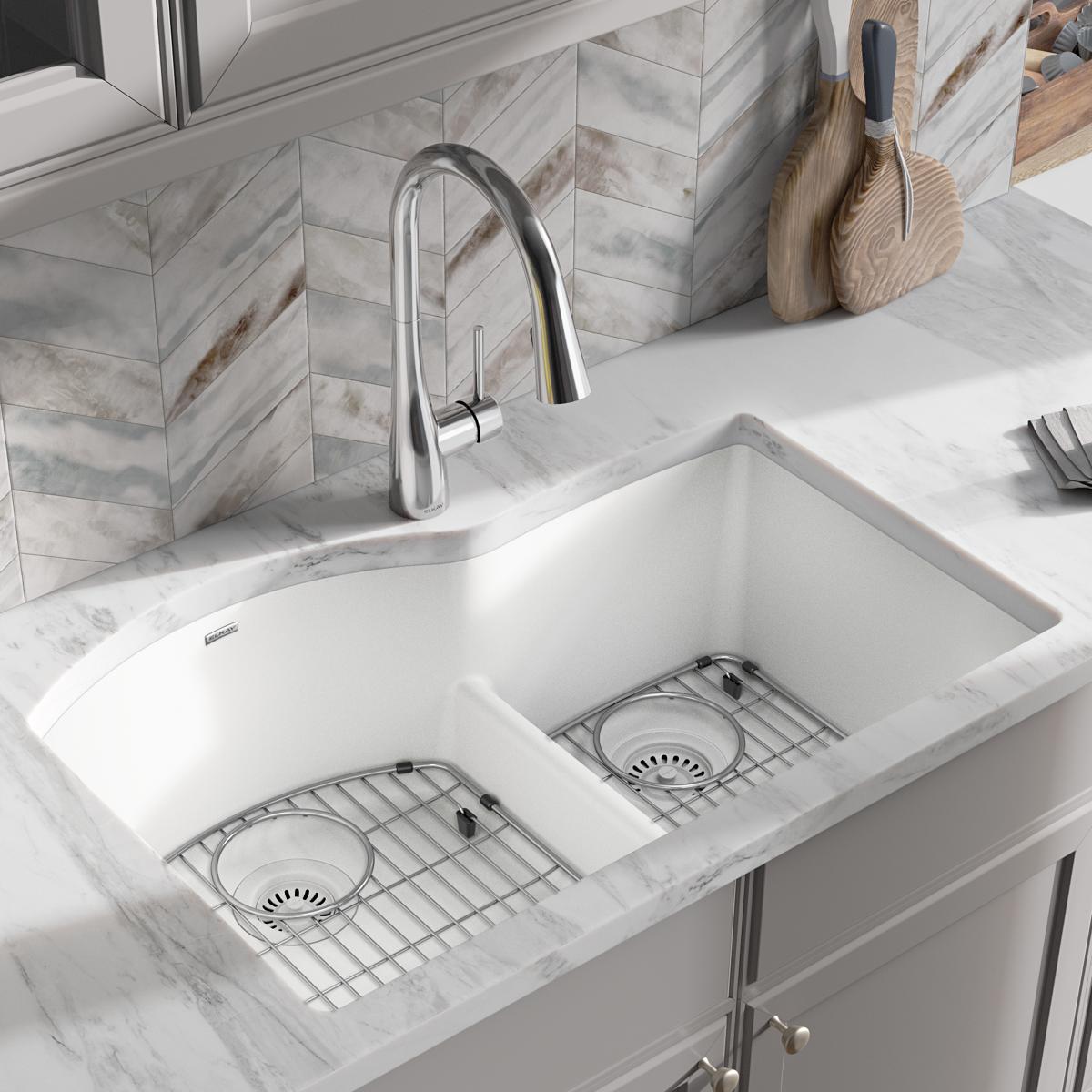 White quartz double bowl undermount sink with offset compartments, stainless steel grid inserts, and divider in marble counte