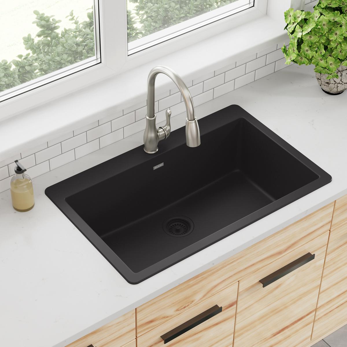 Black quartz single bowl drop-in sink installed in white countertop with stainless steel faucet.