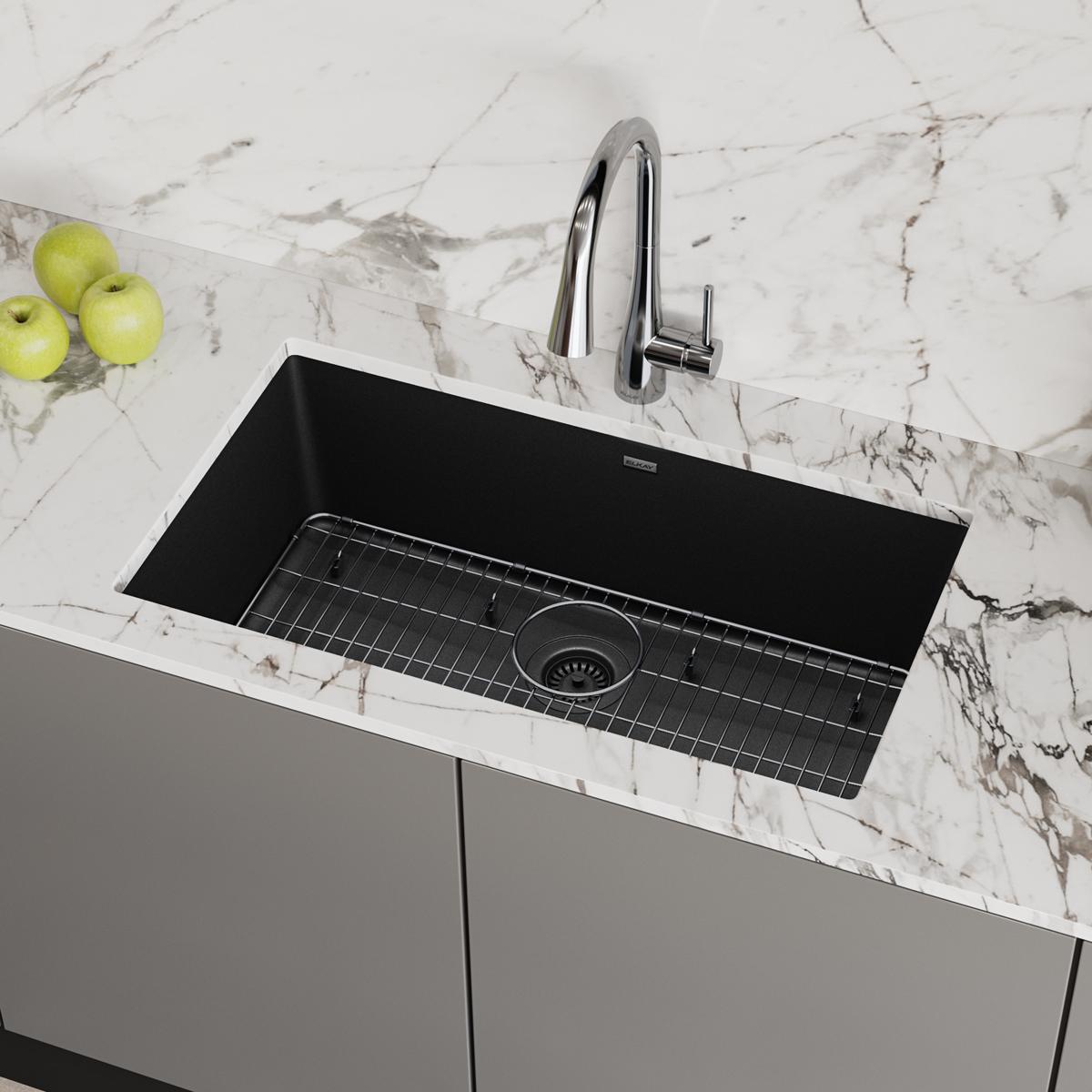 Black quartz undermount sink with single bowl, chrome faucet, and grid strainer installed in marble countertop.