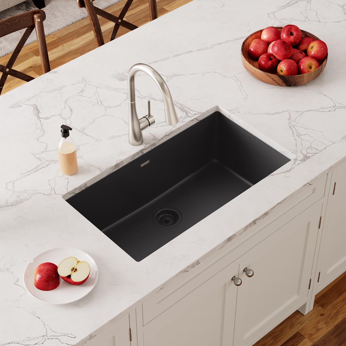 Black quartz undermount sink installed in white marble countertop with stainless steel faucet.