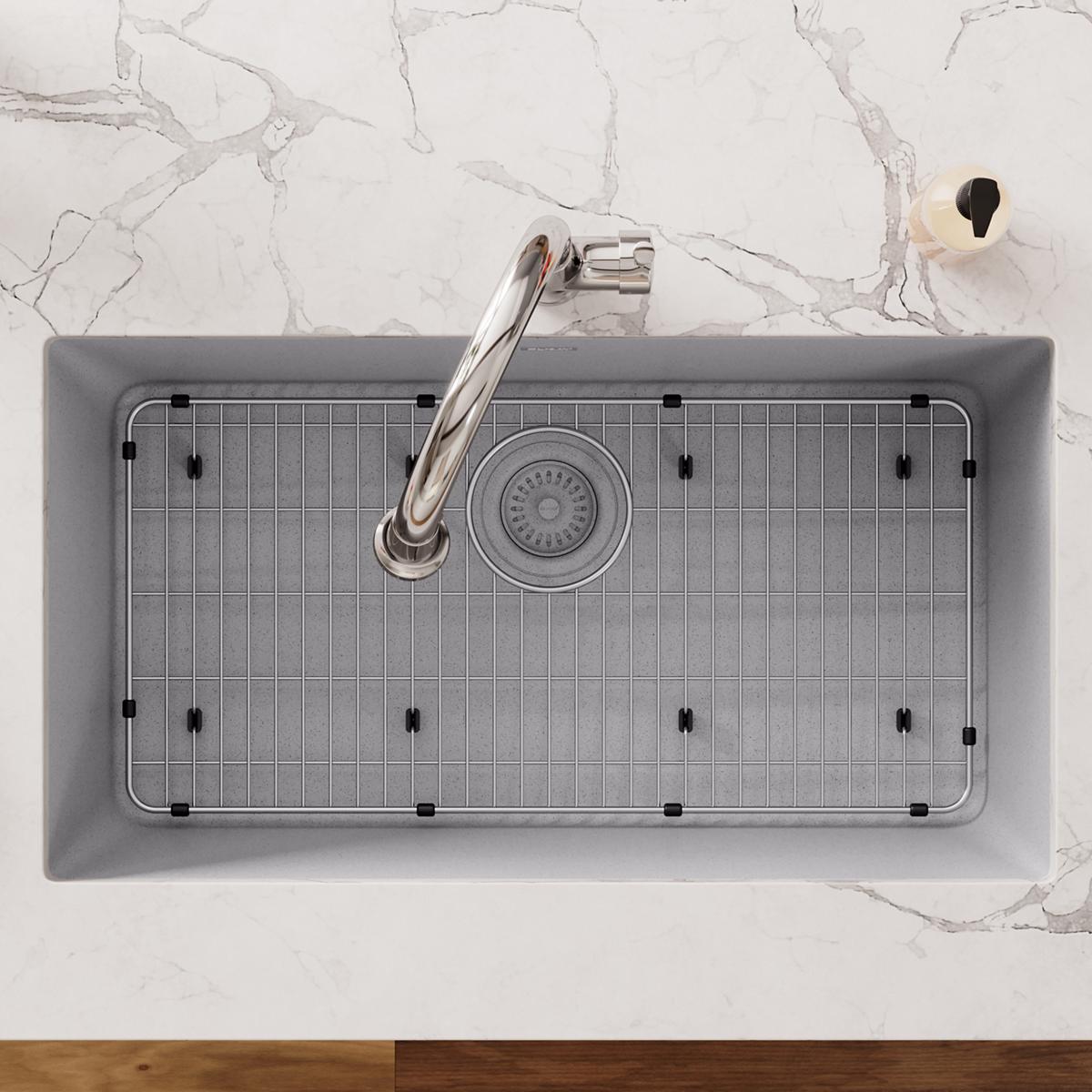 Stainless steel sink grid with vertical lines and black rubber feet positioned in rectangular sink basin with faucet.