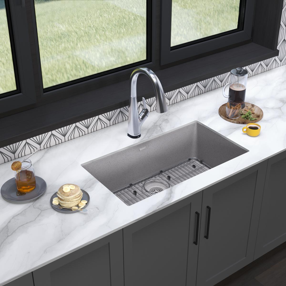 Greystone quartz undermount sink with single bowl and chrome filtered faucet installed in white marble countertop.