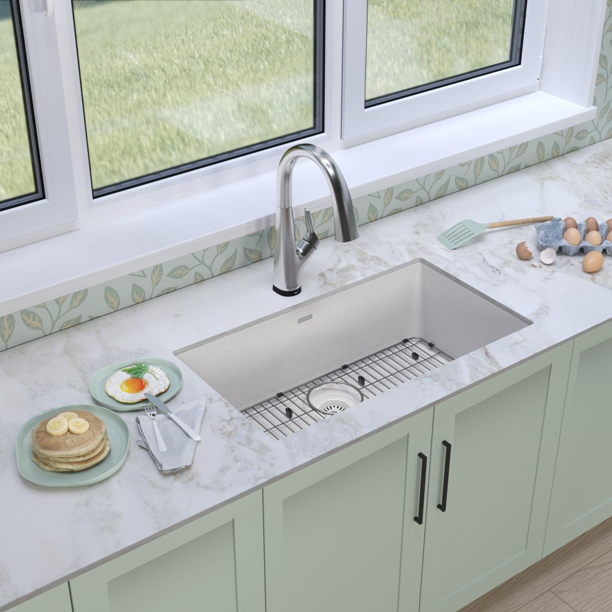 White quartz undermount sink with single bowl, stainless steel faucet, and grid accessory installed in marble countertop.