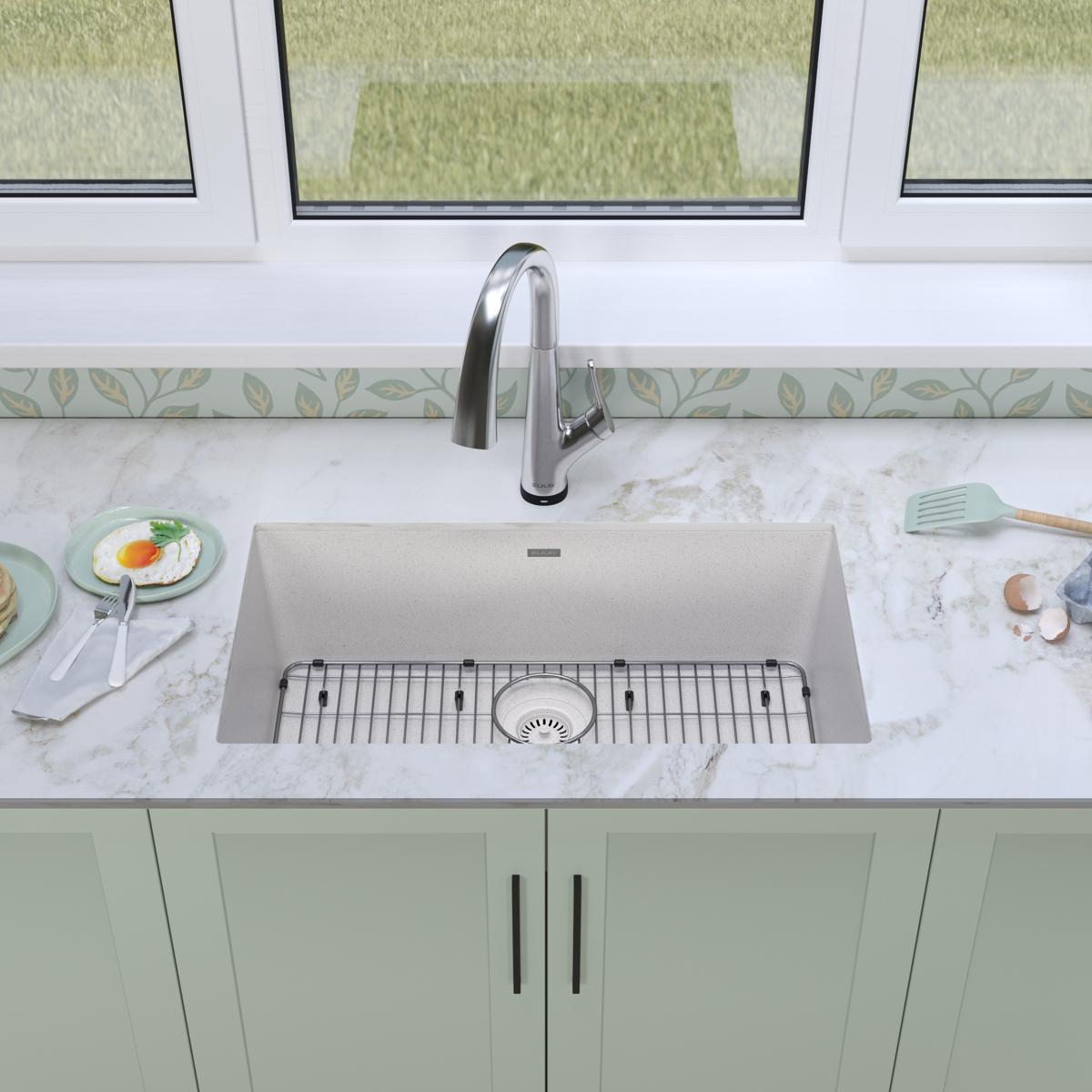 White quartz undermount sink with single bowl, stainless steel faucet, and included grid strainer on marble countertop.