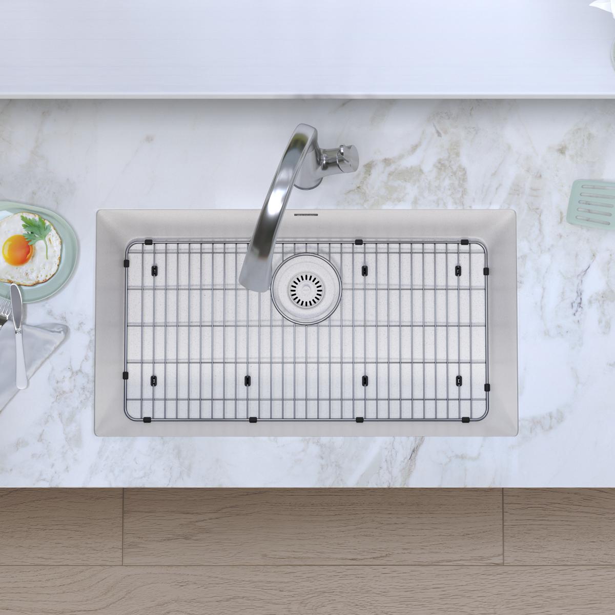 White quartz single bowl undermount sink with stainless steel faucet and grid insert, installed in marble countertop.
