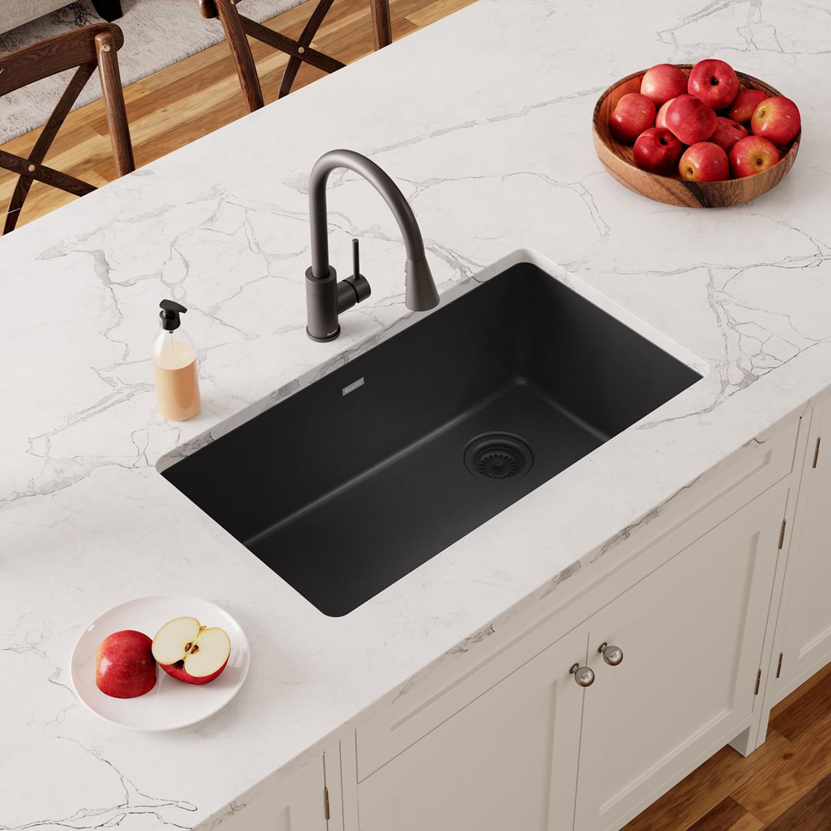 Black quartz undermount sink installed in white marble countertop with black faucet and surrounding kitchen items.