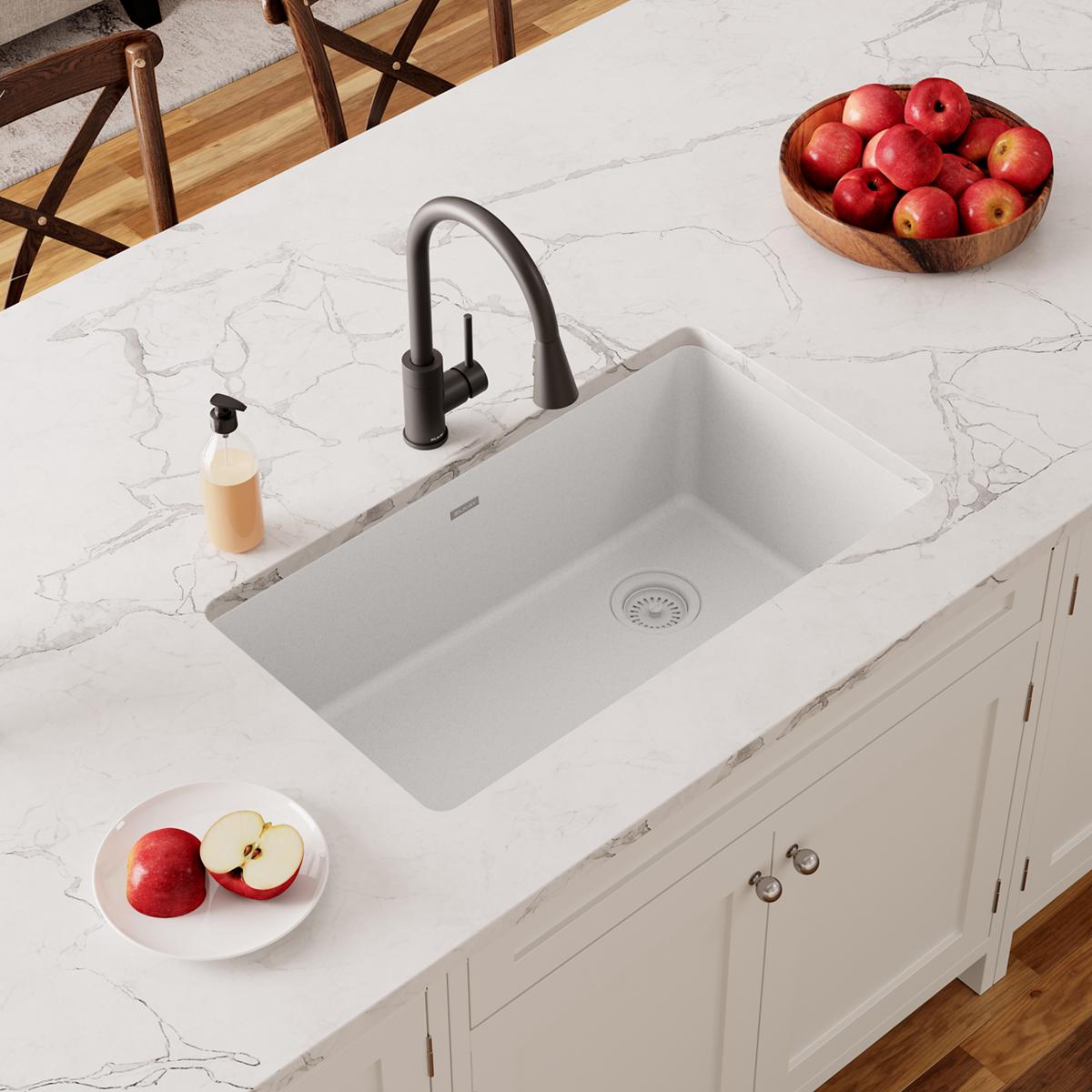 White quartz single bowl undermount sink installed in marble countertop with black faucet.