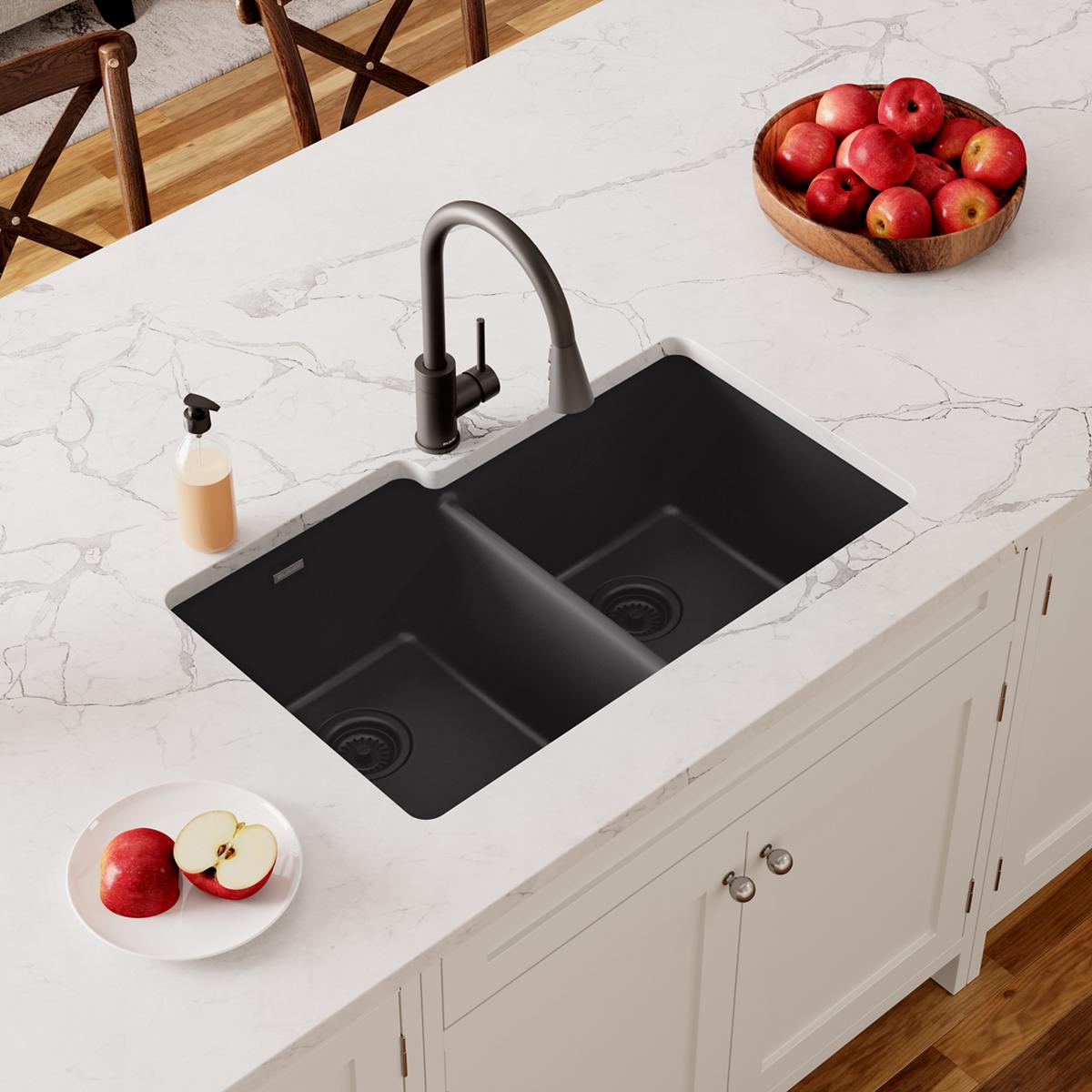 Black quartz undermount kitchen sink with two unequal bowls installed in white countertop with black faucet.