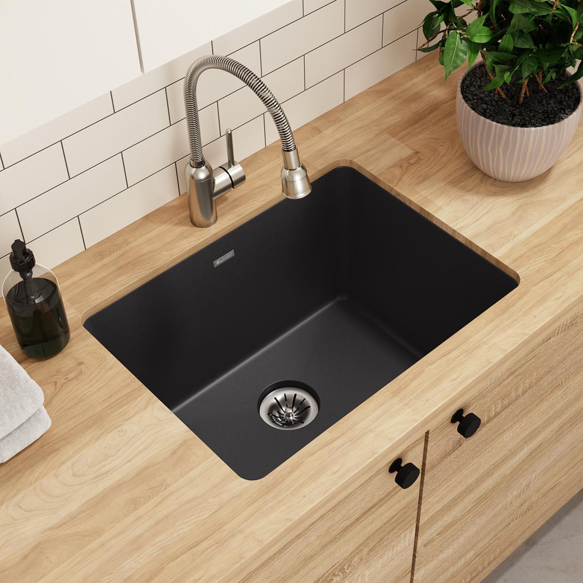 Black quartz undermount laundry sink with single drain installed in wood countertop with faucet.
