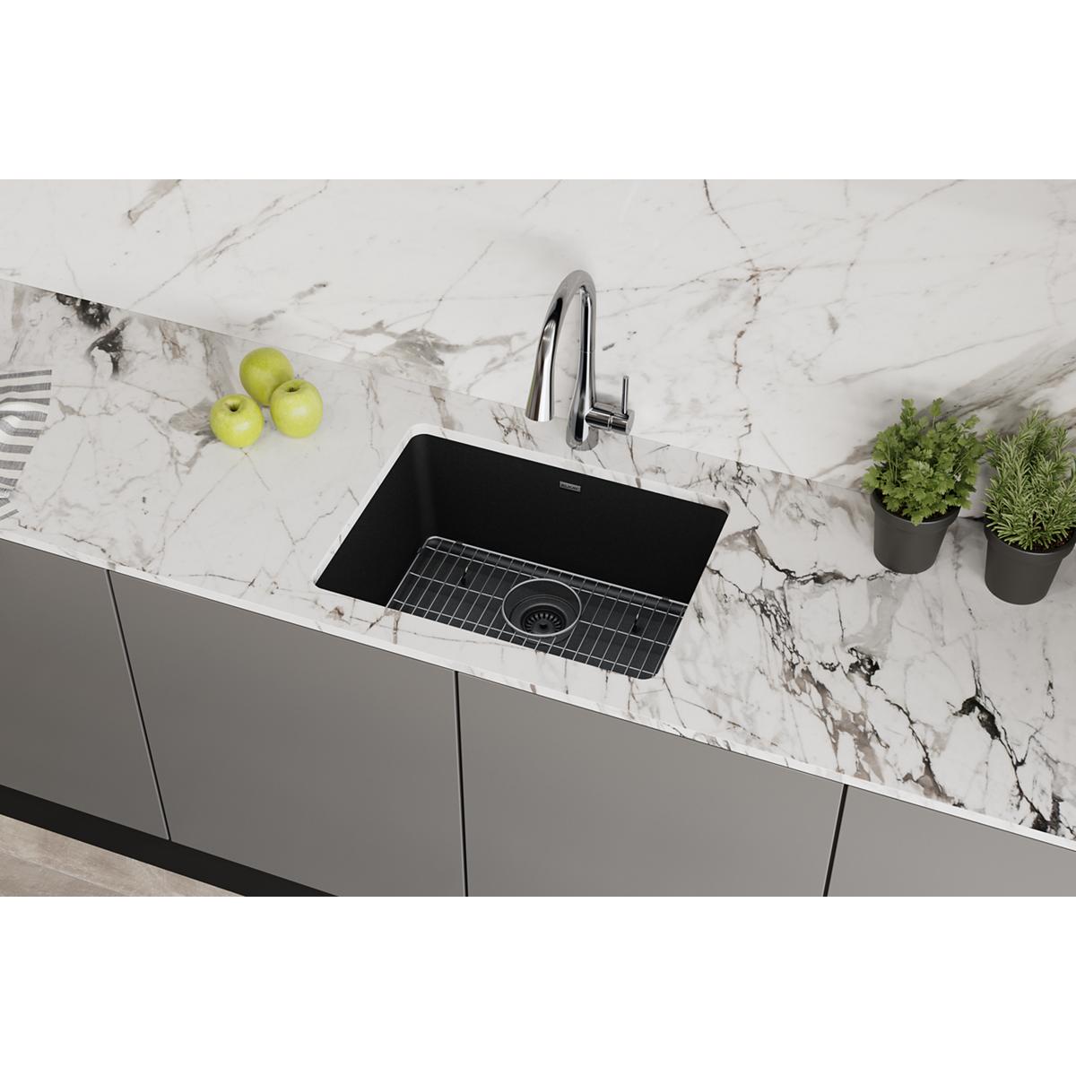 Black quartz undermount kitchen sink with single bowl, chrome faucet, and grid strainer installed in marble countertop.
