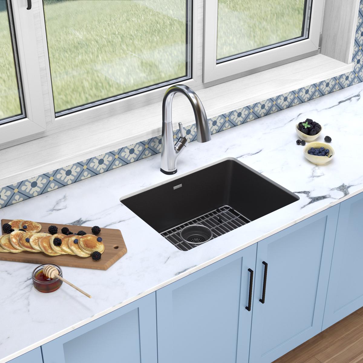 Black quartz undermount kitchen sink with single bowl, stainless steel faucet, and grid strainer installed in white counterto