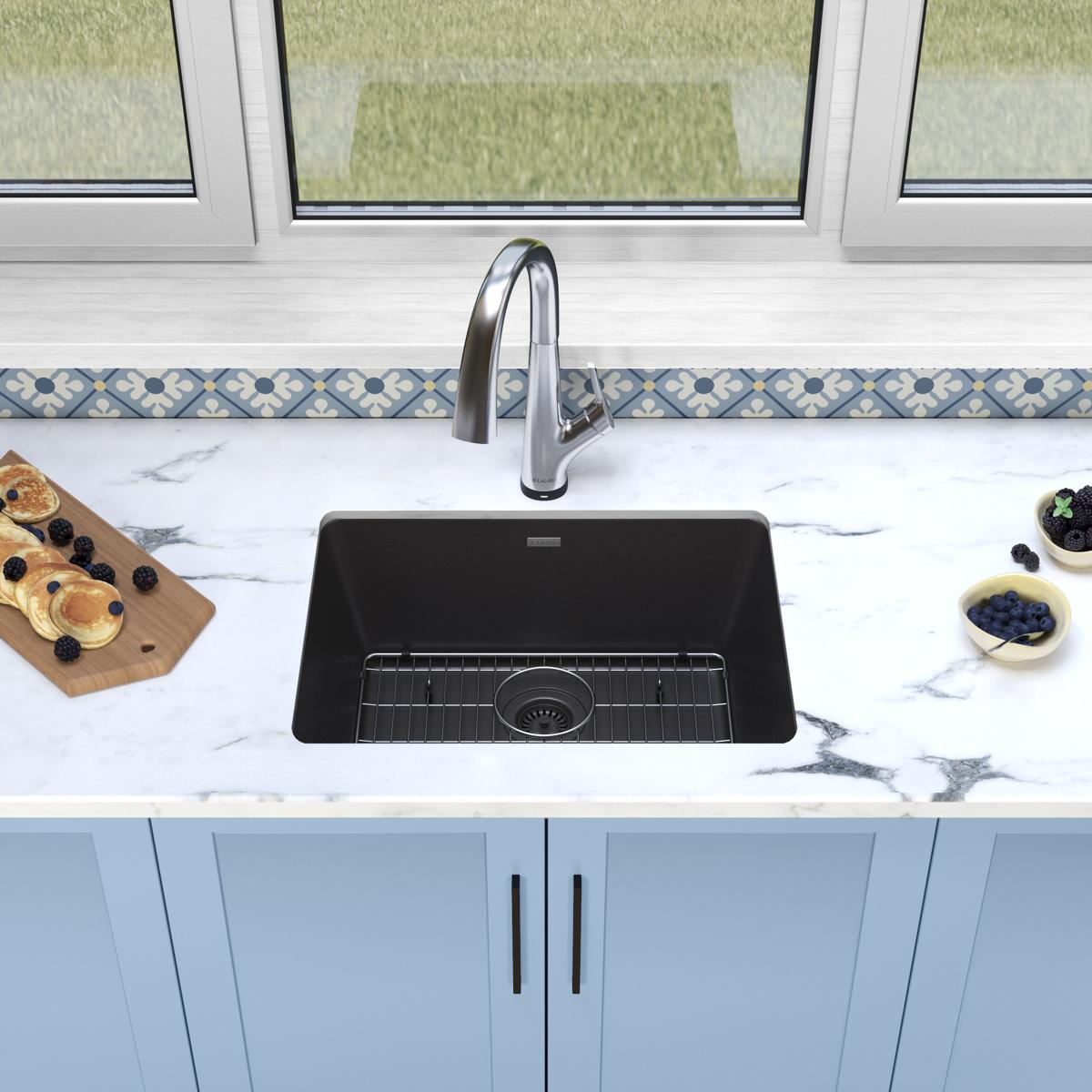 Black quartz undermount sink with single bowl and stainless steel filtered faucet installed in marble countertop.
