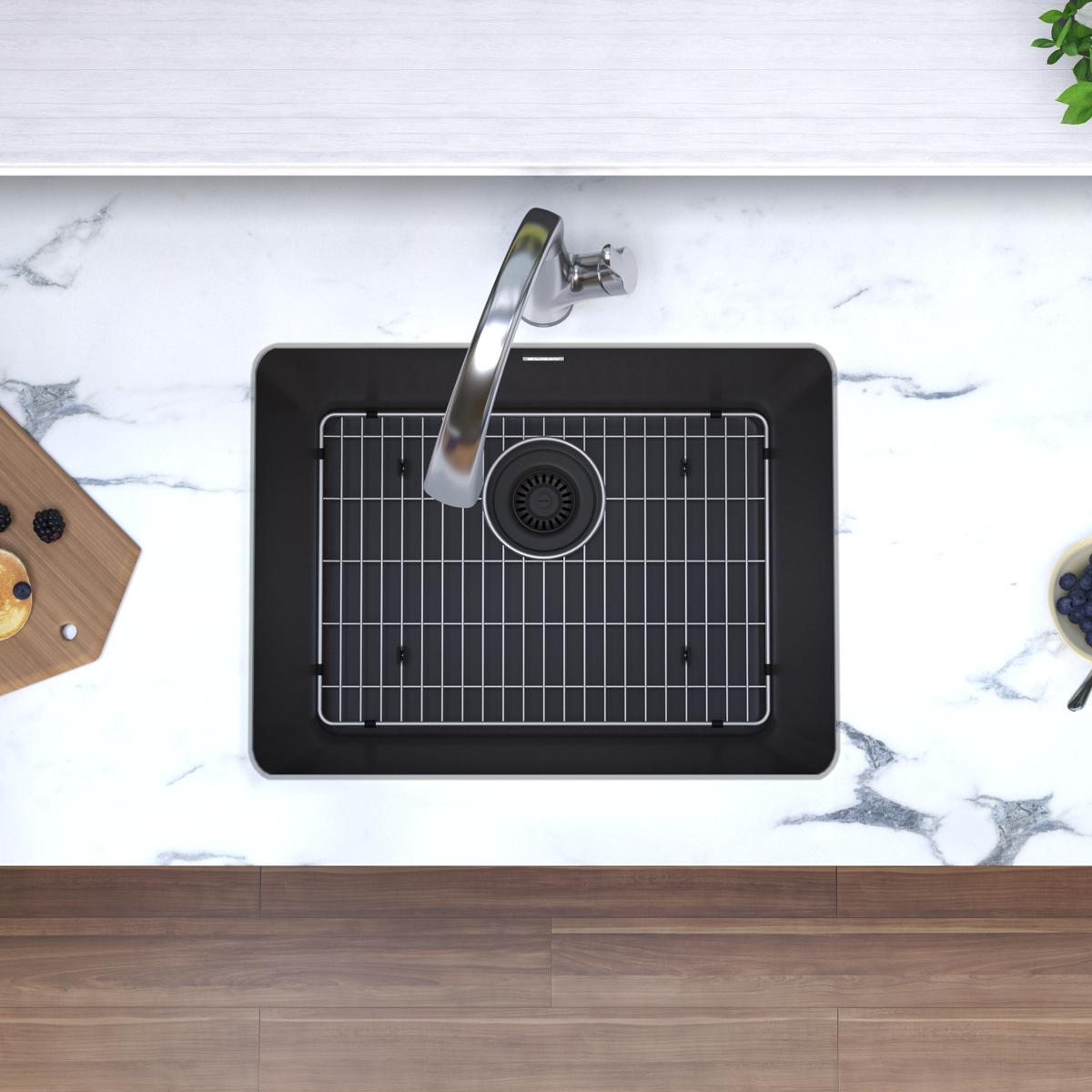 Black quartz undermount sink with stainless steel faucet and grid insert installed in marble countertop.