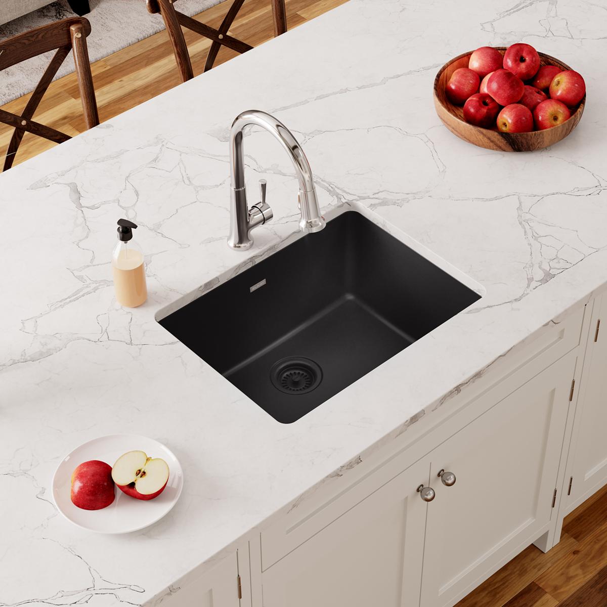 Black quartz undermount sink installed in white marble countertop with chrome faucet and drain.