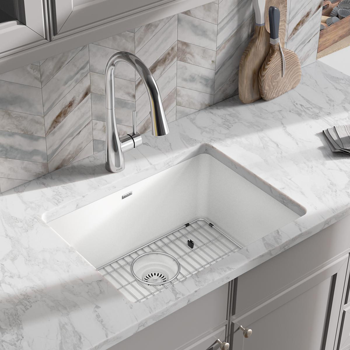 White quartz undermount sink with single bowl, grid strainer, and chrome pull-down faucet installed in marble countertop.