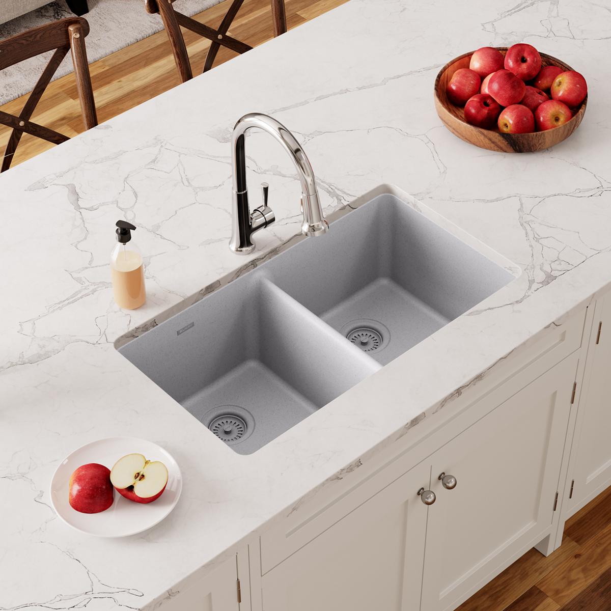 Greystone quartz double bowl undermount sink installed in white marble countertop with chrome faucet.