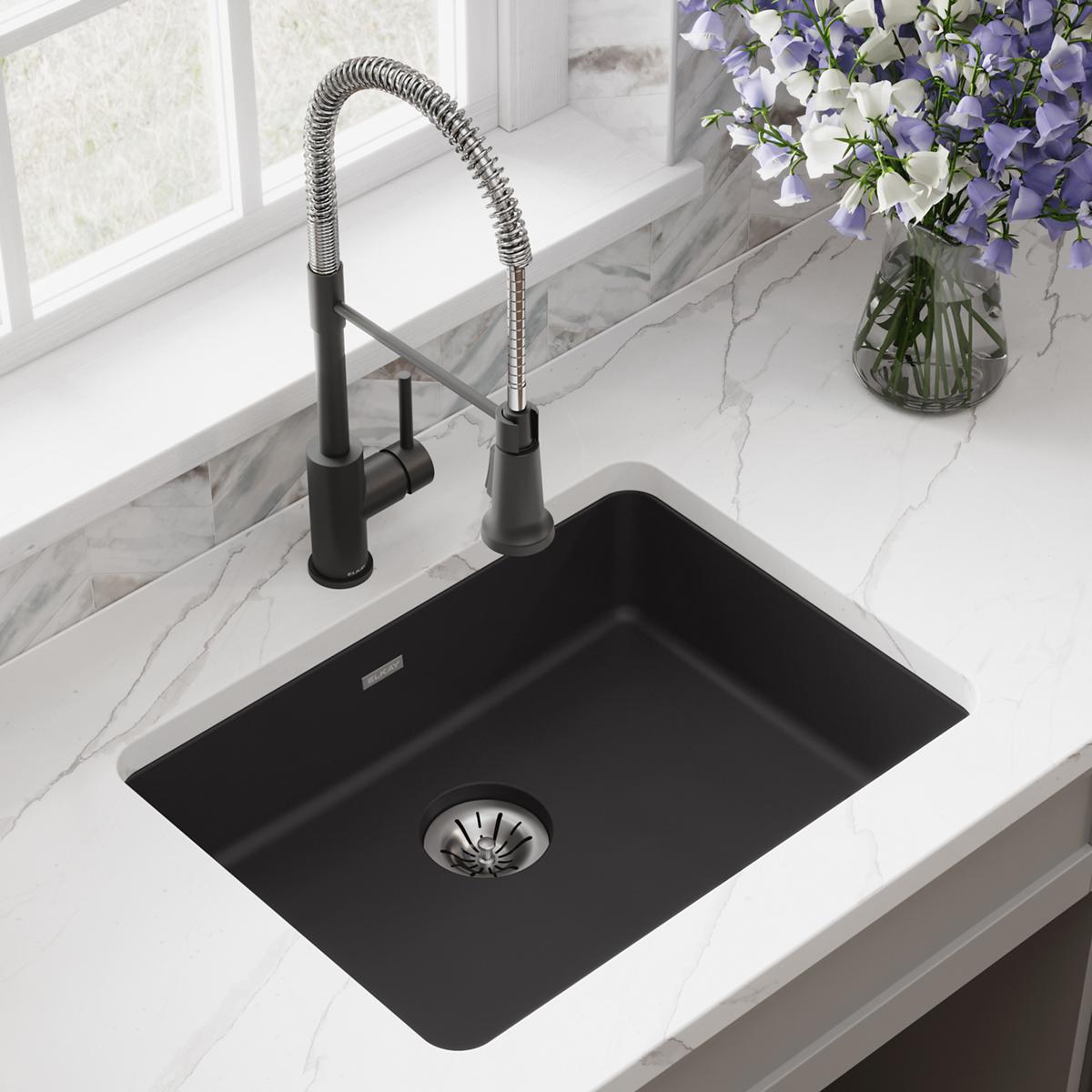 Black quartz undermount sink with single bowl and stainless steel pull-down faucet in marble countertop.