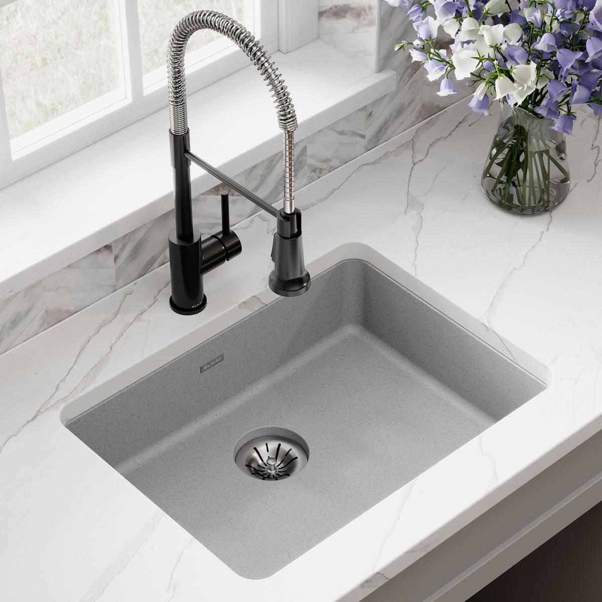 Greystone quartz single bowl undermount sink with black pull-down faucet installed in marble countertop.