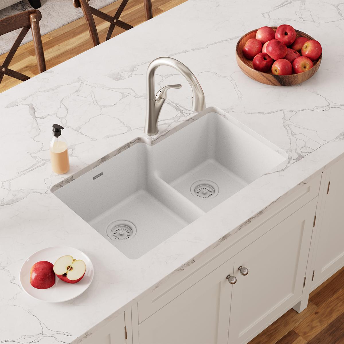 White quartz undermount sink with two unequal bowls, divider, and stainless steel faucet on marble countertop.