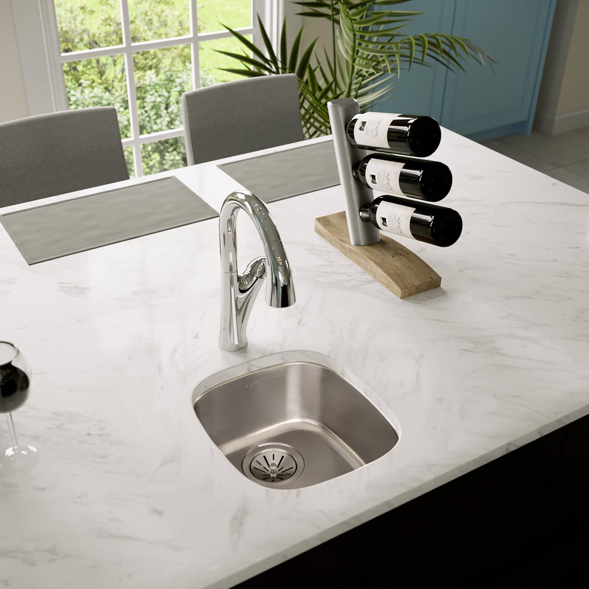 Stainless steel single bowl undermount sink installed in white marble countertop with chrome faucet.