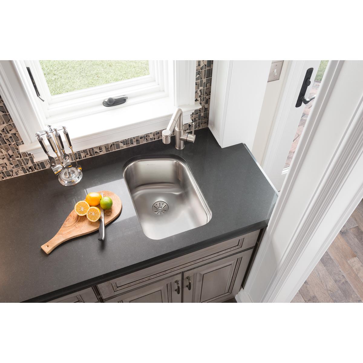 Stainless steel single bowl undermount sink installed in black countertop with drain visible at bottom.