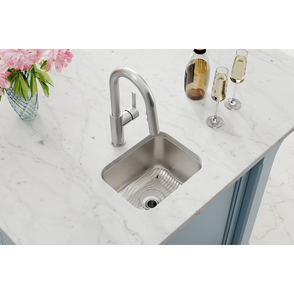 Stainless steel undermount bar sink with single bowl, matching faucet, and grid strainer installed in marble countertop.