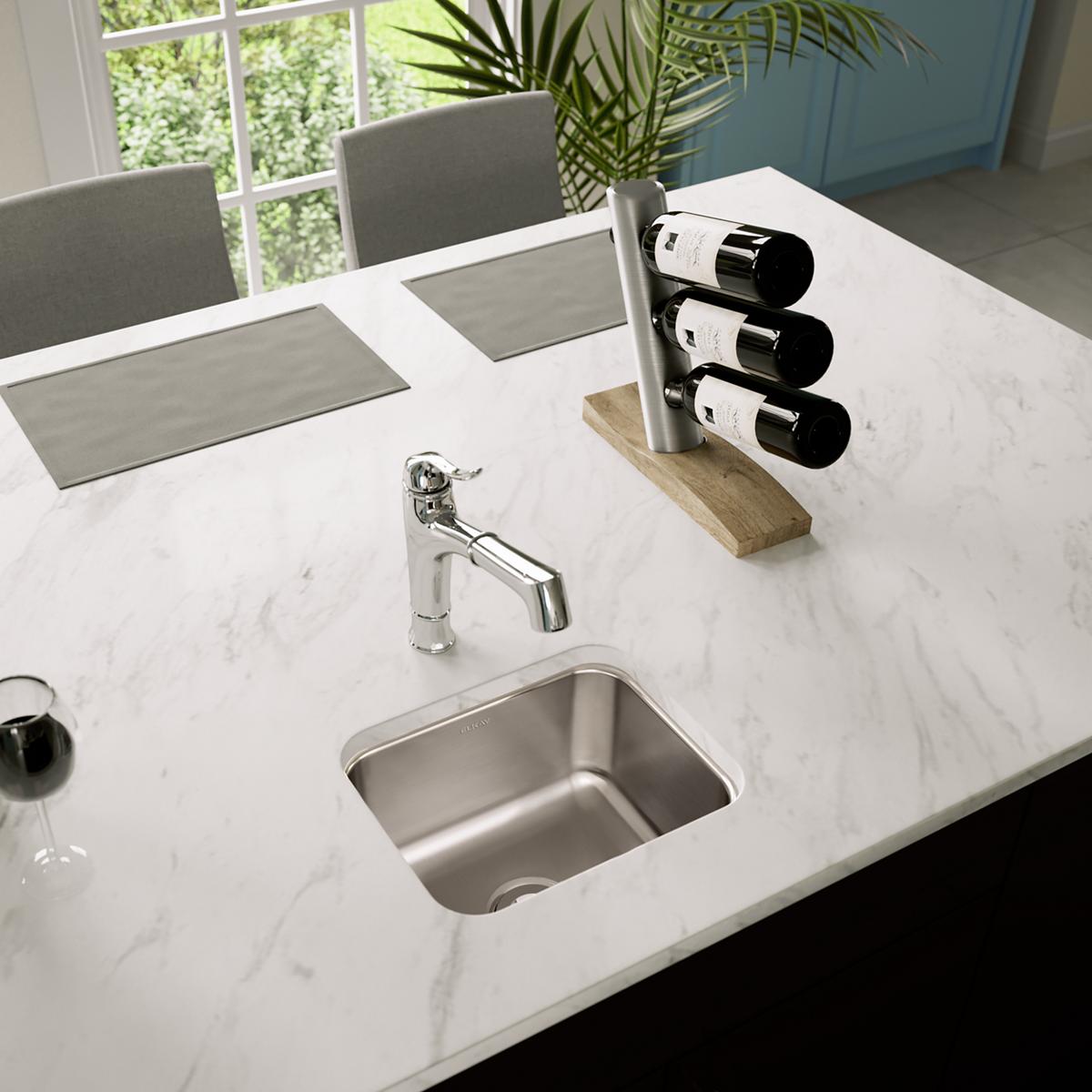 Stainless steel single bowl undermount sink installed in white marble countertop with chrome faucet.
