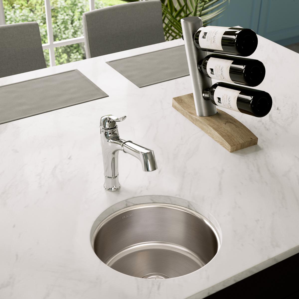Stainless steel round undermount sink installed in white marble countertop with chrome faucet.
