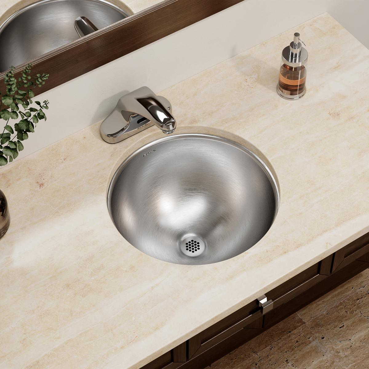Stainless steel round undermount bathroom sink installed in light marble countertop with chrome faucet and drain visible.