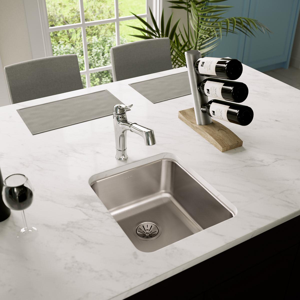 Stainless steel single bowl undermount sink installed in white marble countertop with chrome faucet.