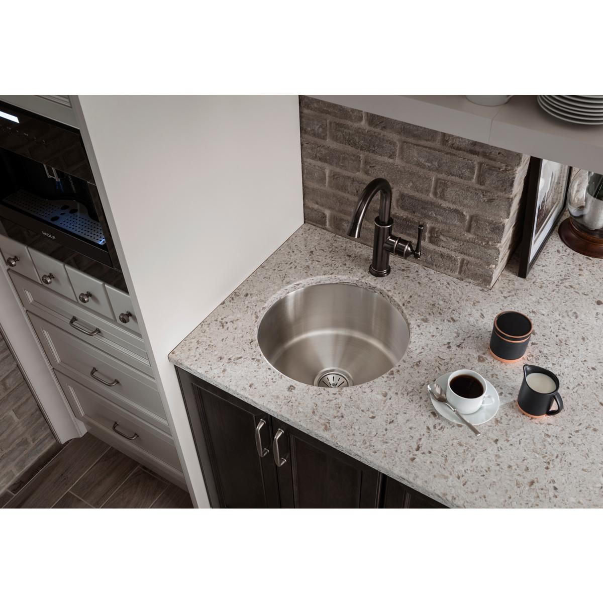 Antique steel single-hole bar faucet with forward lever handle installed above round stainless steel sink on granite countert
