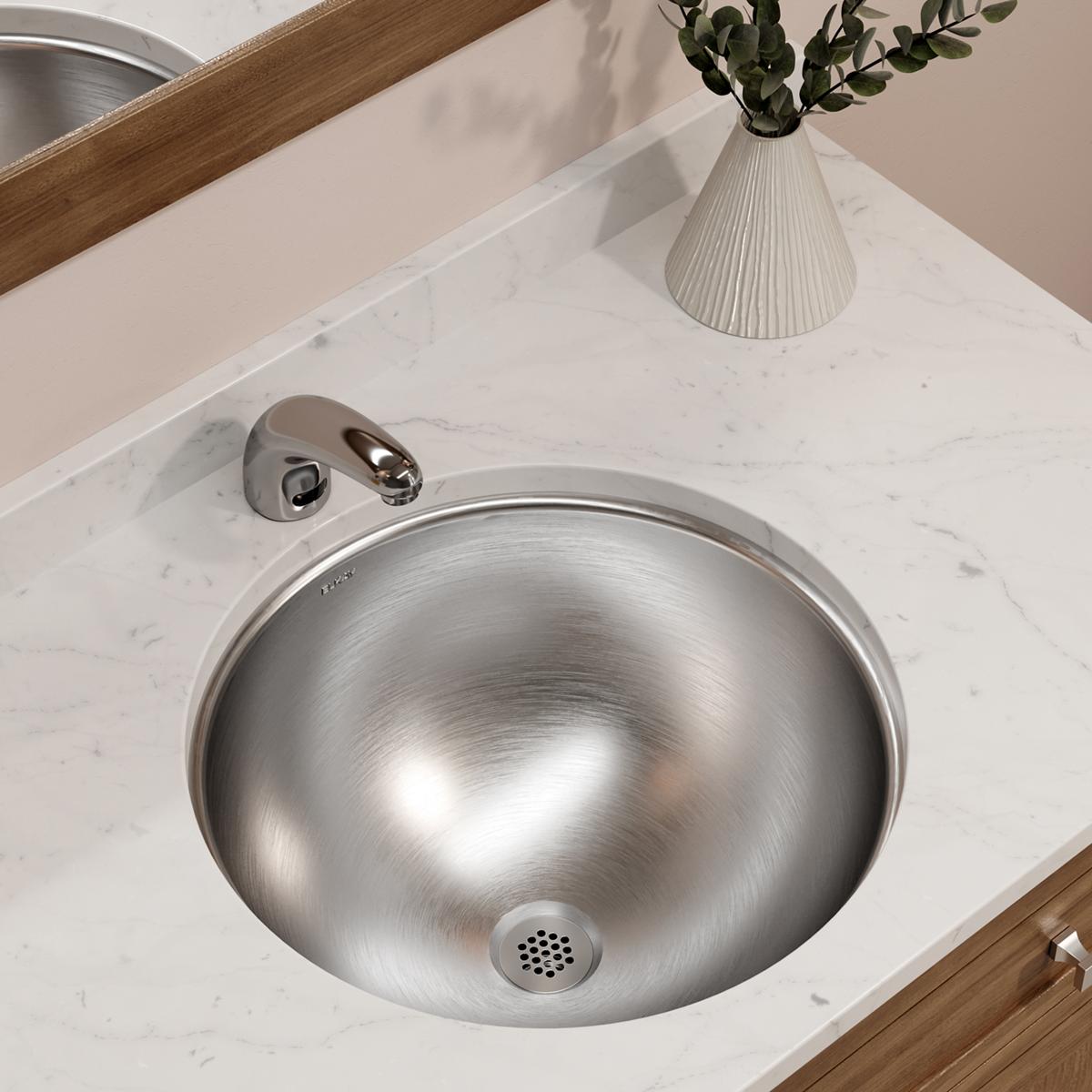 Stainless steel round undermount bathroom sink installed in marble countertop with chrome faucet and overflow drain.