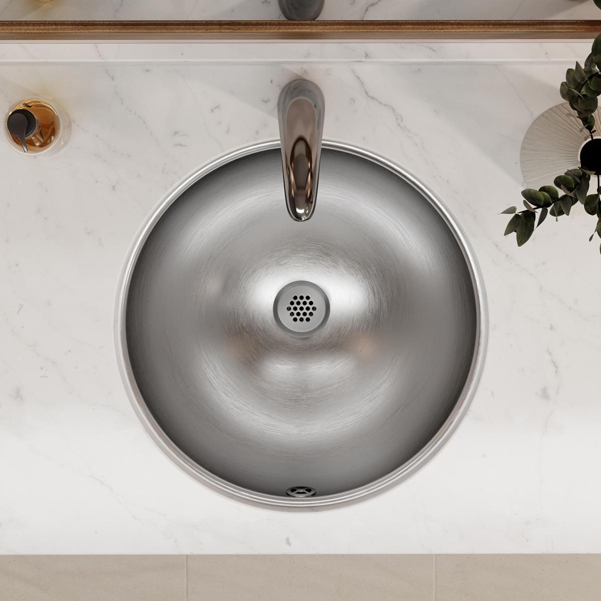Stainless steel round bathroom sink with overflow hole, mounted beneath marble countertop with faucet and drain visible.