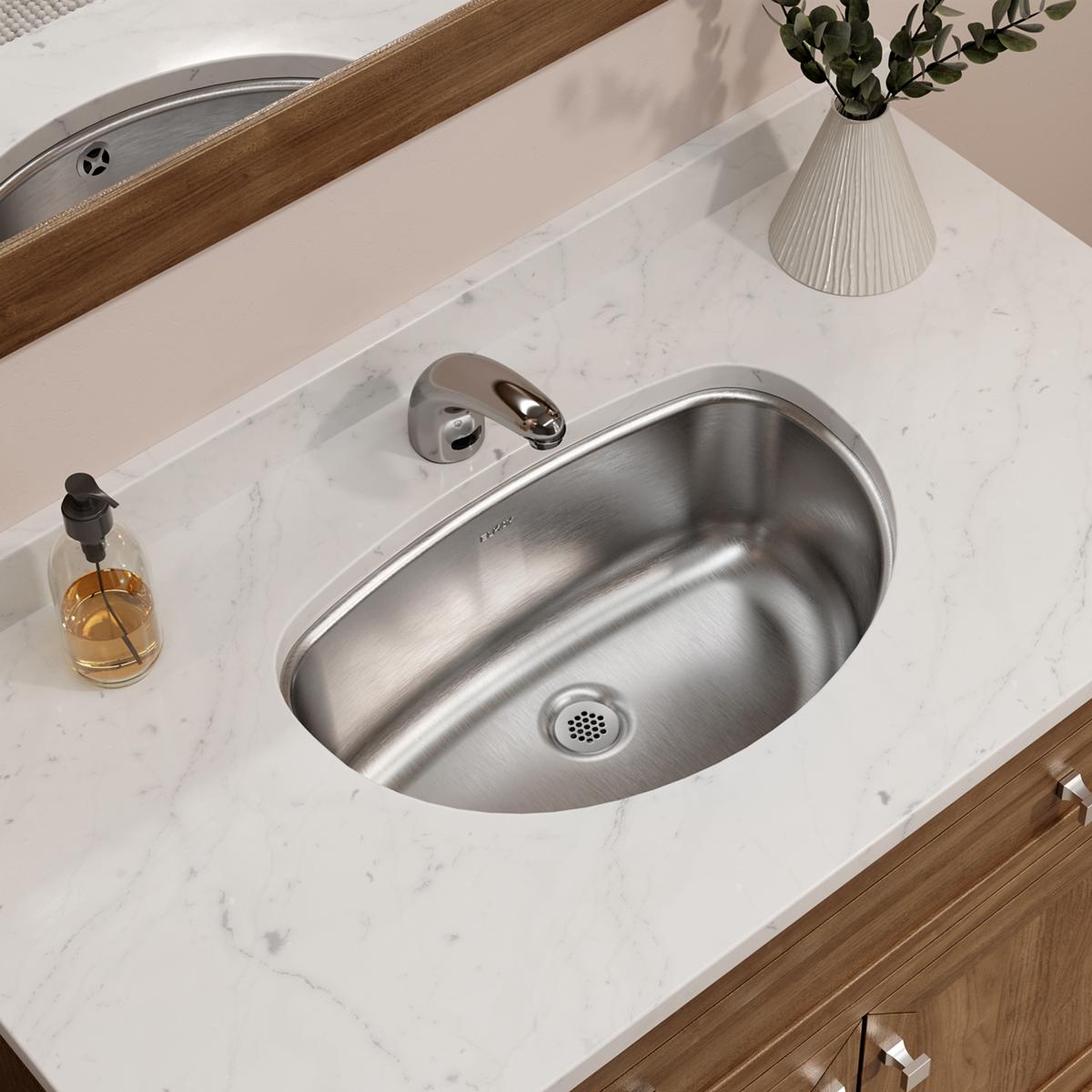 Stainless steel undermount bathroom sink with oval bowl installed in white marble countertop, wall-mounted faucet visible.