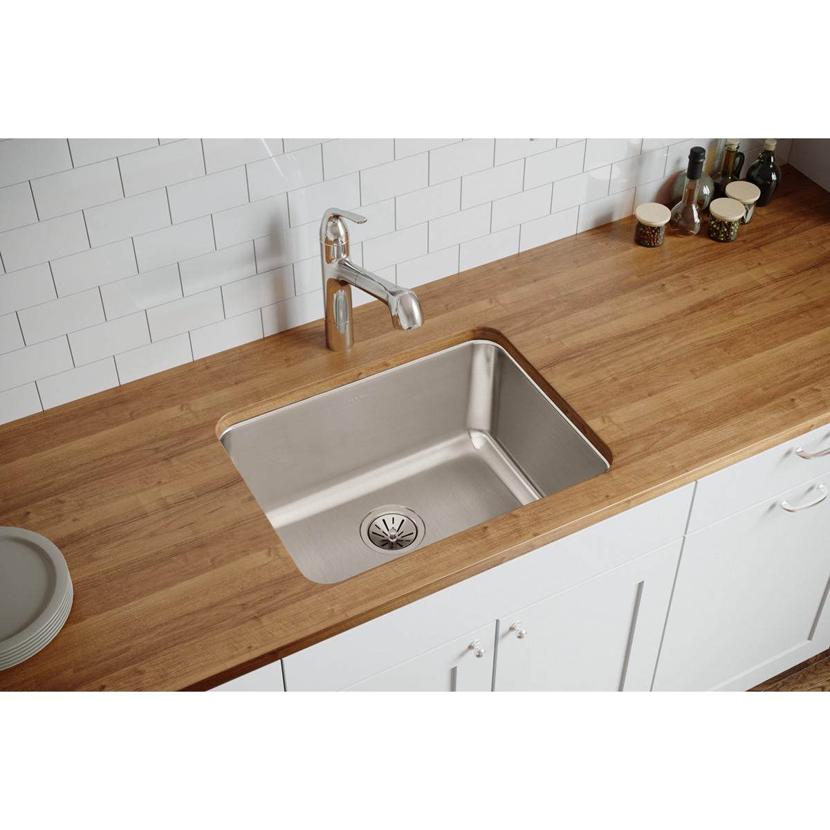 Stainless steel single bowl undermount sink installed in wooden countertop with chrome faucet and white subway tile backsplas