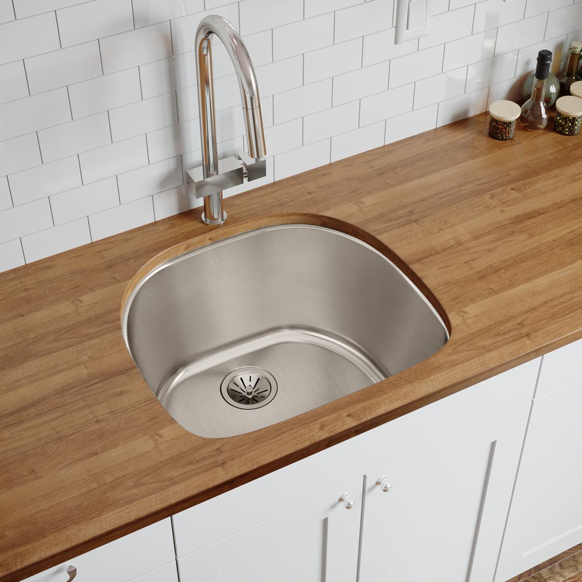 Stainless steel single bowl undermount sink installed in wood countertop with chrome faucet and white subway tile backsplash.