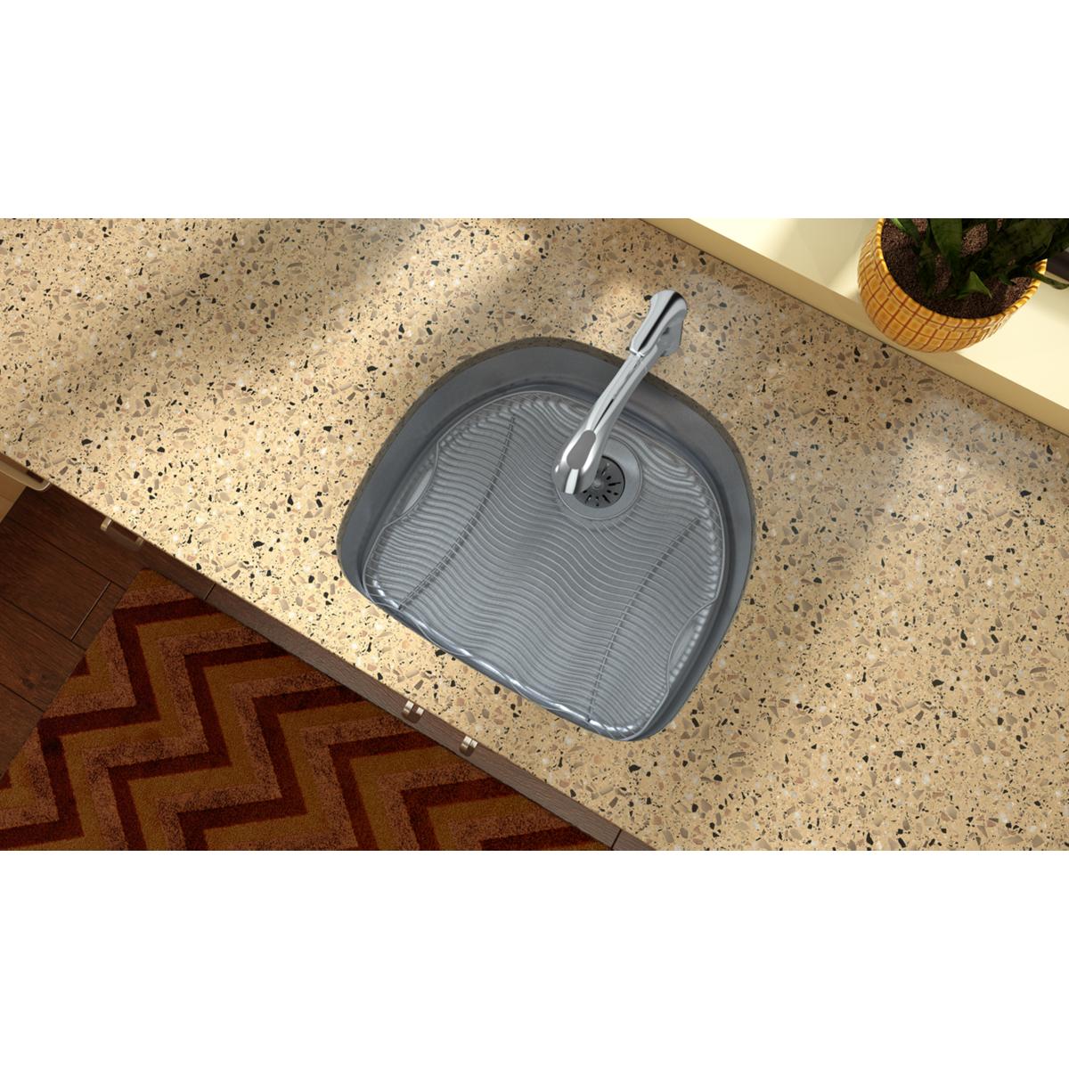 Stainless steel single bowl undermount sink with ribbed basin and chrome faucet installed in quartz countertop.