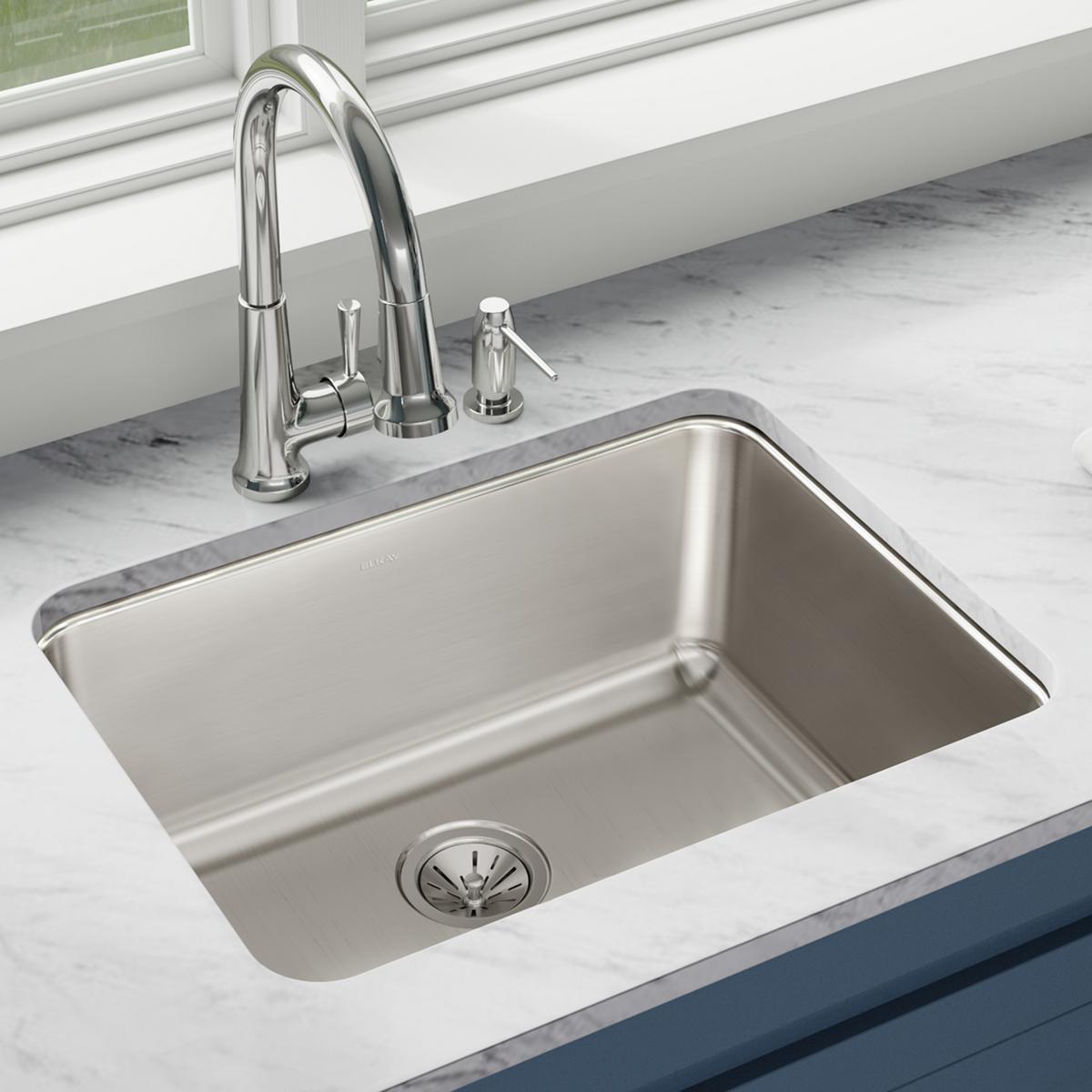 Stainless steel single bowl undermount sink installed in marble countertop with chrome faucet and soap dispenser.