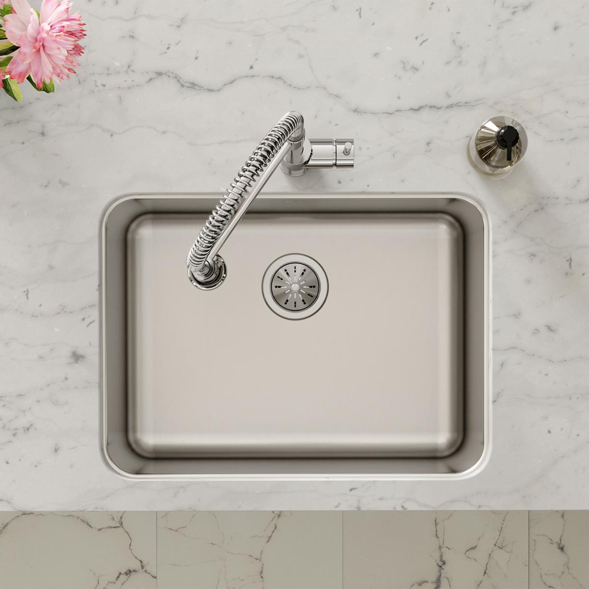 Stainless steel undermount sink with rounded corners, drain strainer, and flexible spray faucet installed in marble counterto