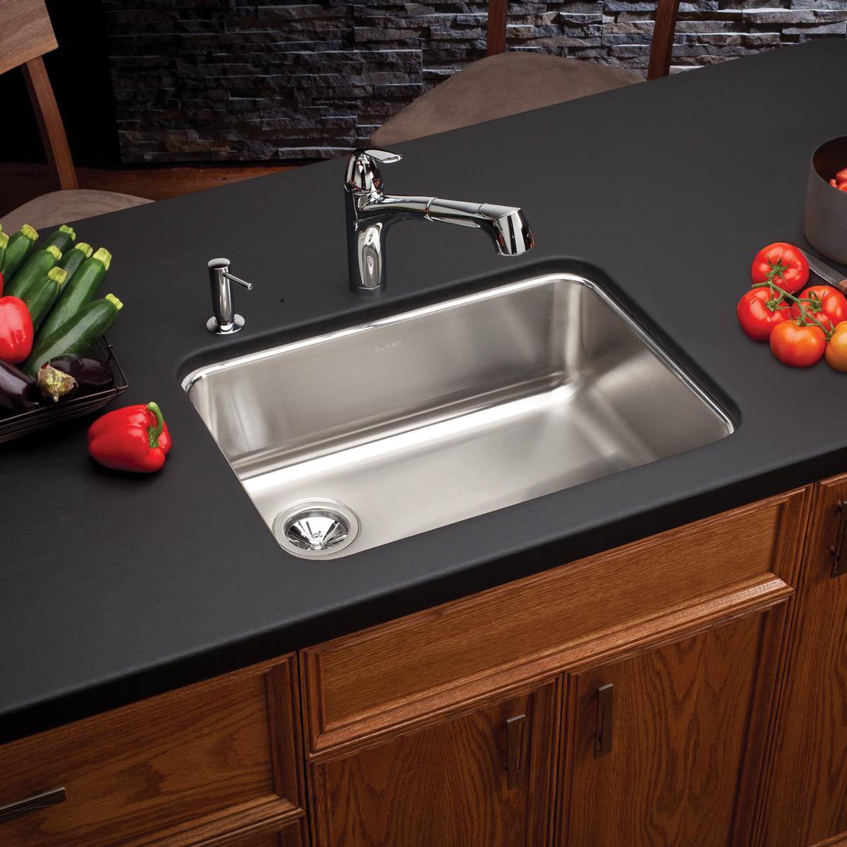 Stainless steel single bowl undermount sink with left drain installed in dark countertop with chrome faucet.