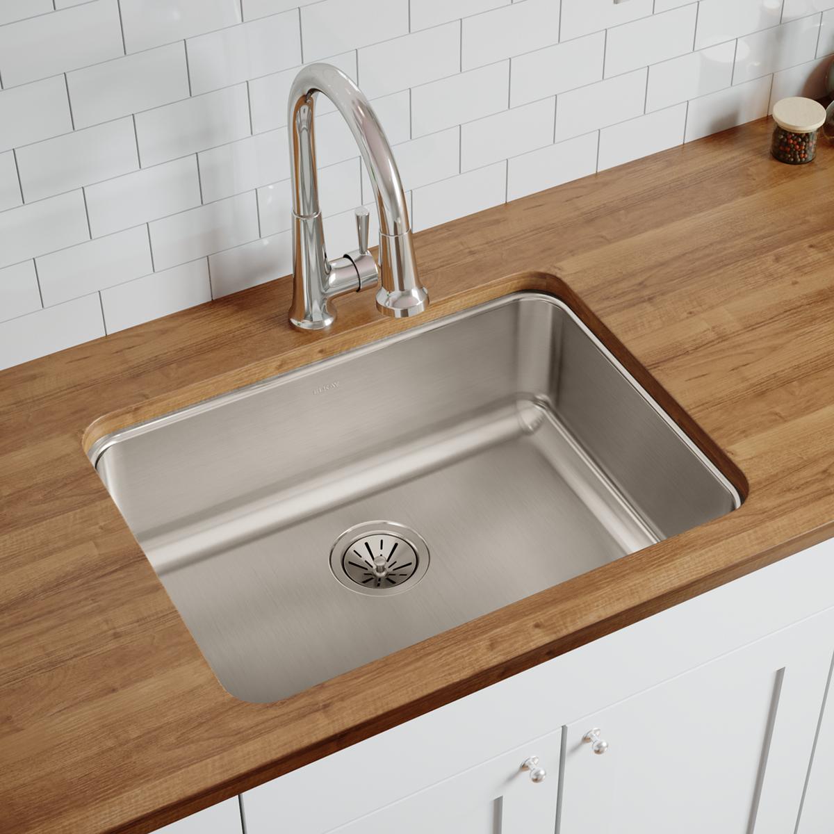 Stainless steel single bowl undermount sink installed in wood countertop with chrome faucet and white subway tile backsplash.
