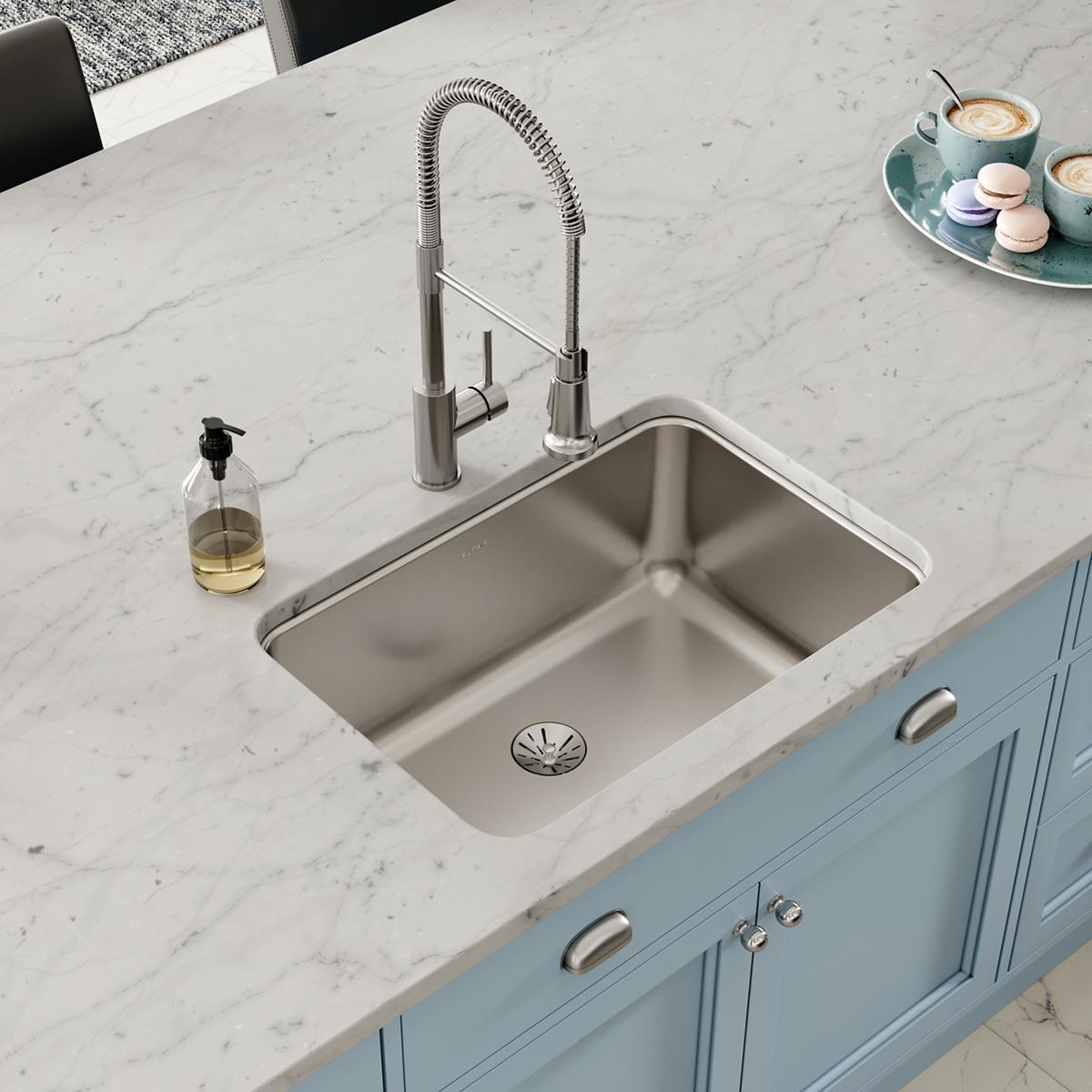 Stainless steel undermount sink installed in marble countertop with spray faucet and drain strainer visible.