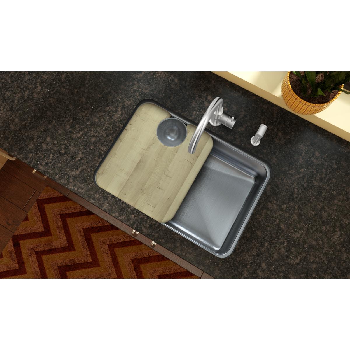 Light wood cutting board with groove positioned next to stainless steel sink bowl on dark countertop.
