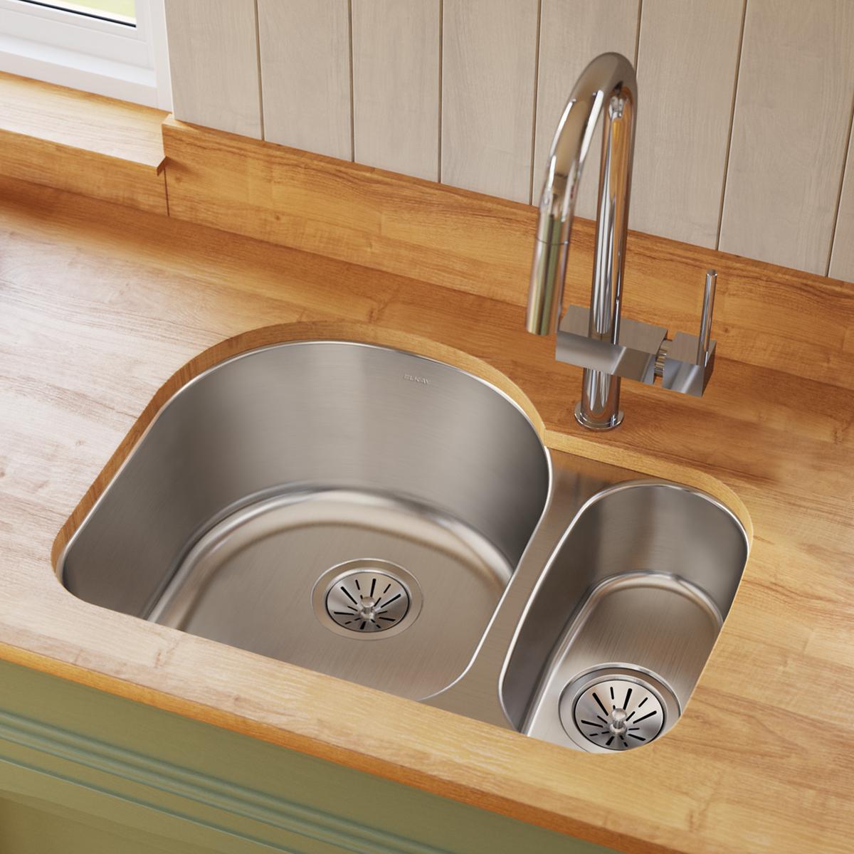 Stainless steel double bowl undermount sink with offset 70/30 configuration installed in wood countertop with chrome faucet.