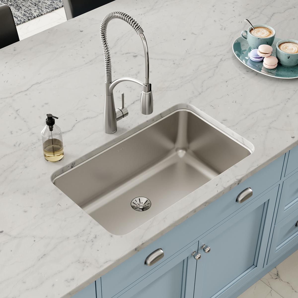 Stainless steel single bowl undermount sink installed in white marble countertop with sprayer faucet.