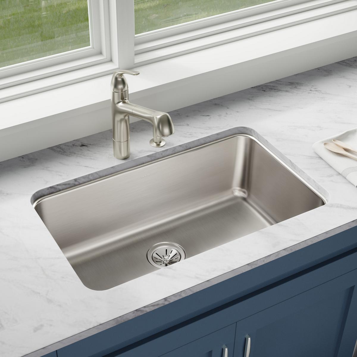 Stainless steel single bowl undermount sink installed in white marble countertop with faucet and drain visible.