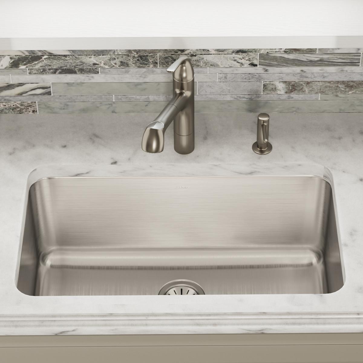 Stainless steel single bowl undermount sink installed in marble countertop with brushed nickel faucet and soap dispenser.