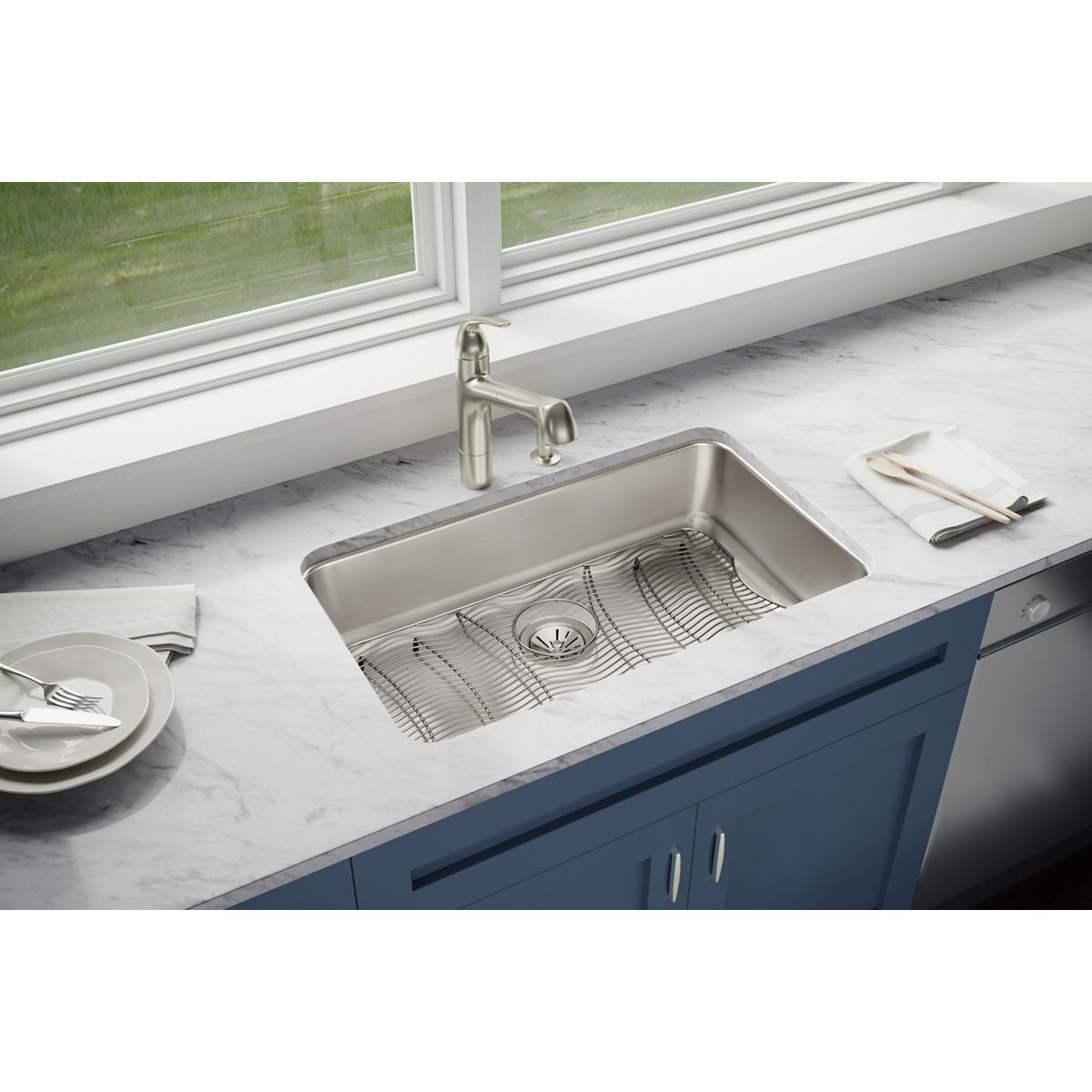 Stainless steel undermount sink with single bowl, drain, and metal grid insert installed in white countertop.